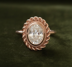 Rose gold oval ring with twisted rope halo on dark olive green velvet