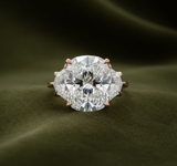 Rose gold three-stone ring with oval center and pentagon sides on dark olive green velvet